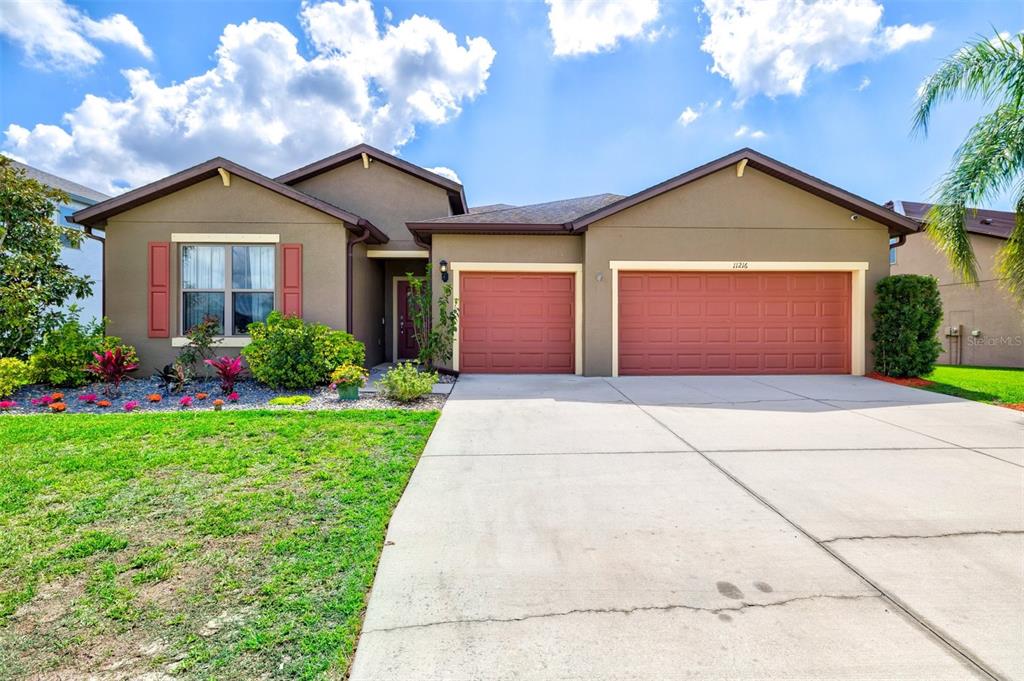 A single-story house with a three-car garage, brown stucco exterior, and red shutters — 11216 58TH STREET CIRCLE E, PARRISH, FL