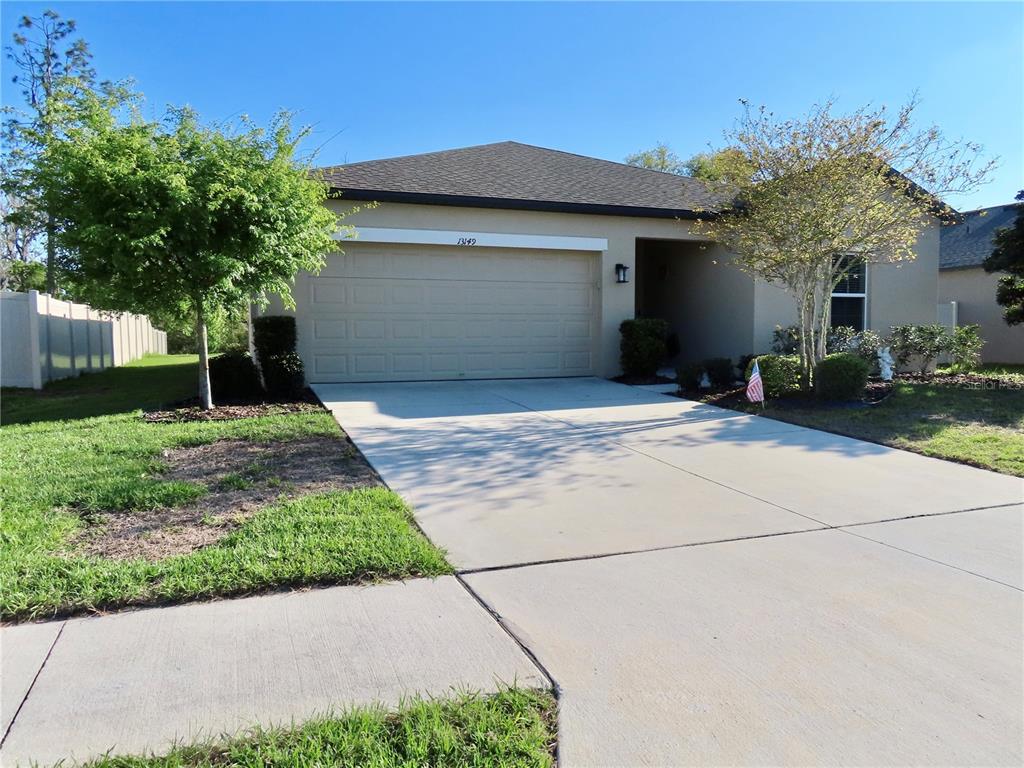 A single-story house with a beige stucco exterior, a two-car garage, and a concrete driveway — 13149 CONQUISTADOR LOOP, SPRING HILL, FL