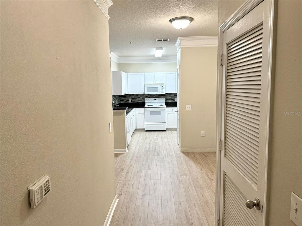 A hallway leads to a kitchen with white cabinets, white appliances, and light wood-look flooring — 8842 VILLA VIEW CIRCLE UNIT 307, ORLANDO, FL