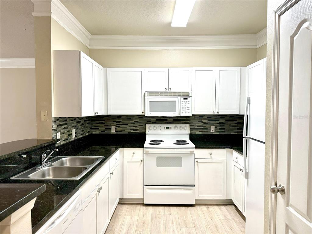 A kitchen features white cabinetry, black countertops, a tiled backsplash, and white appliances — 8842 VILLA VIEW CIRCLE UNIT 307, ORLANDO, FL