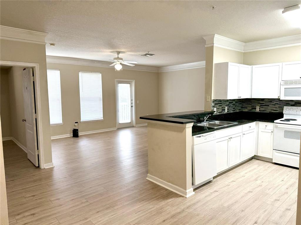 A kitchen with white cabinets and black countertops opens into a living area with wood-look flooring — 8842 VILLA VIEW CIRCLE UNIT 307, ORLANDO, FL