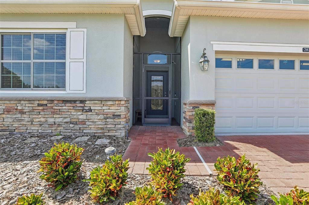 The exterior of a house features a stone-accented facade, a brick walkway, and a screened entryway — 2823 MAYPORT STREET, CLERMONT, FL