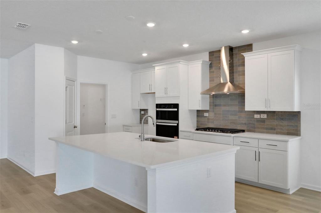 A modern kitchen features white cabinetry, a large quartz island, and a tiled backsplash — 2254 BRANNINGS SAWMILL COURT, MIDDLEBURG, FL