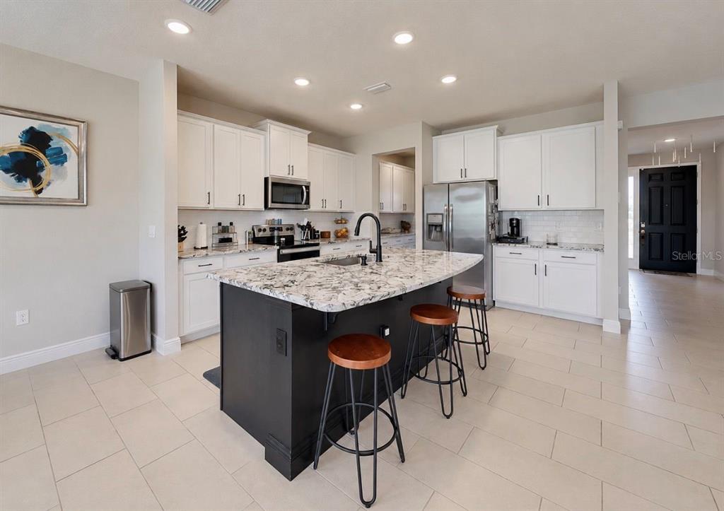 A kitchen features a black island with bar stools, white cabinetry, and stainless steel appliances — 172 MANGROVE MANOR DRIVE, APOLLO BEACH, FL