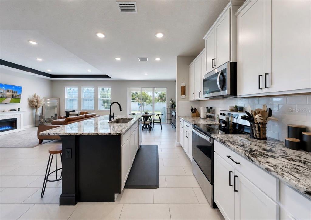 A modern kitchen features white cabinets, granite countertops, a black island, and stainless steel appliances — 172 MANGROVE MANOR DRIVE, APOLLO BEACH, FL