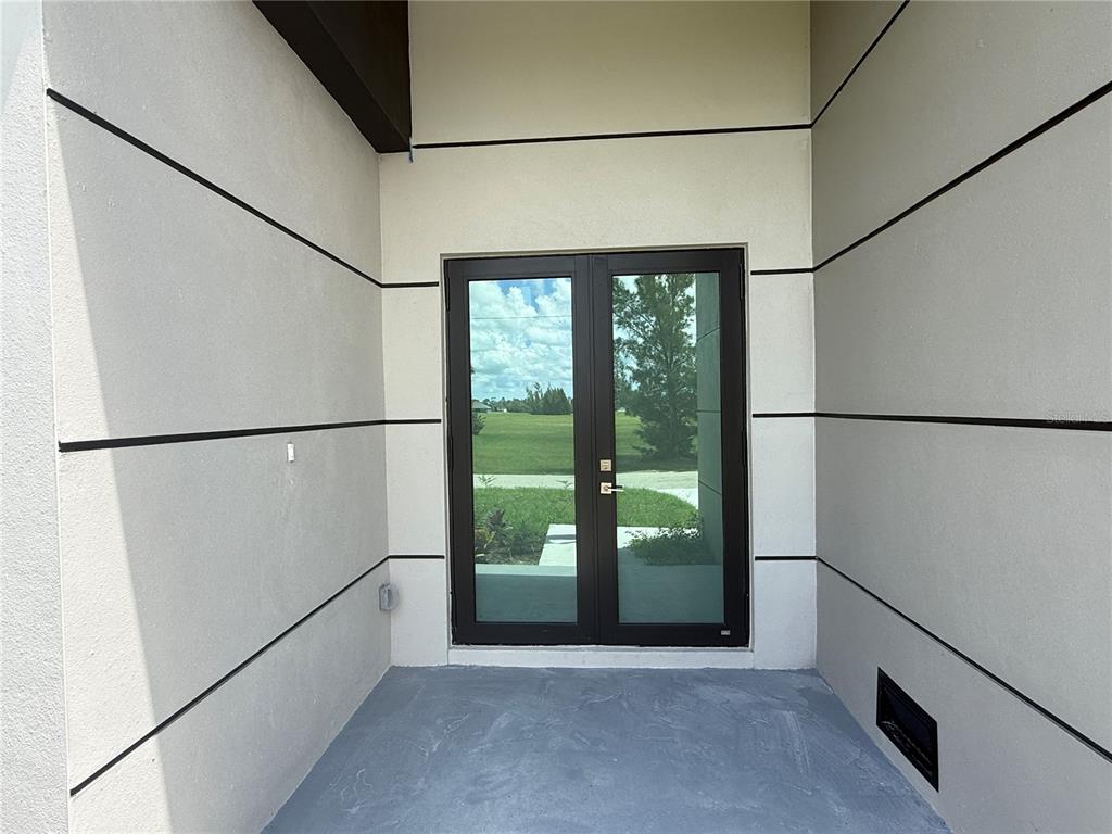 A covered entryway features light-colored walls with horizontal black accents and double glass doors — 4005 NW 22ND STREET, CAPE CORAL, FL