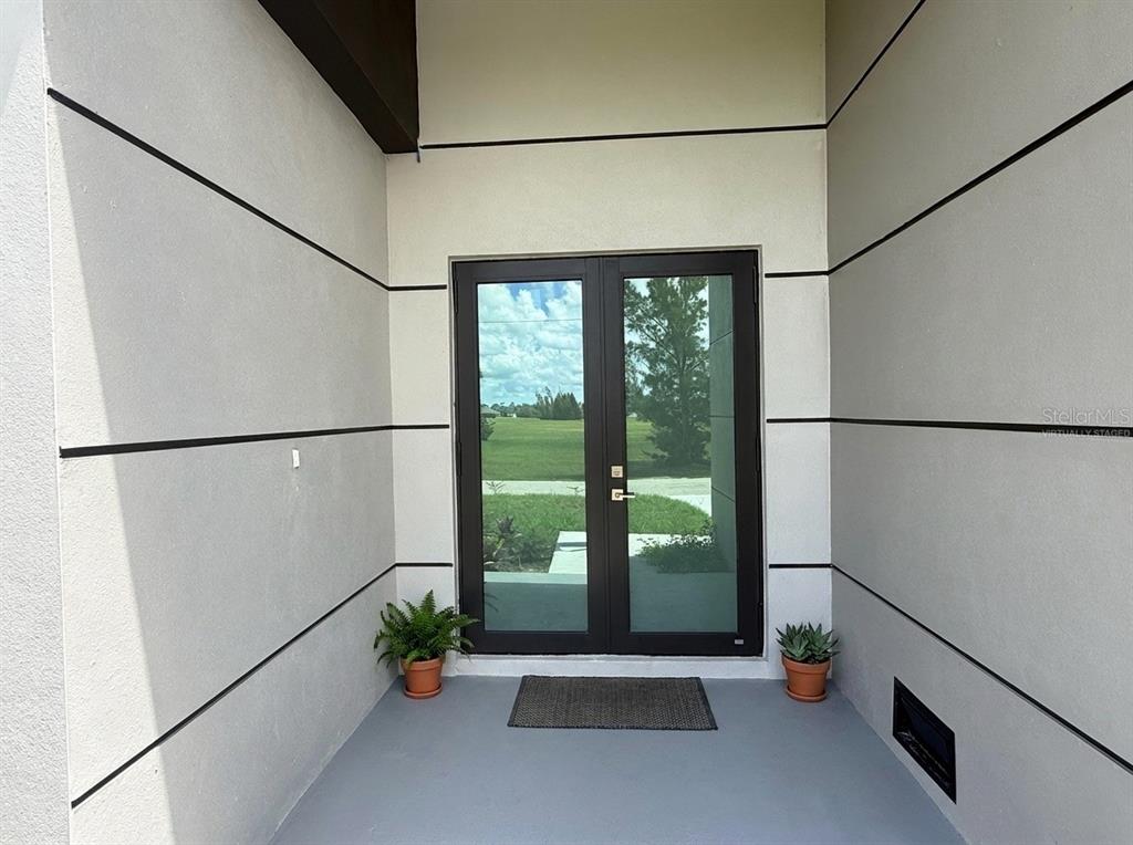 A modern entryway features double glass doors, light-colored walls with horizontal accents, and two potted plants — 4005 NW 22ND STREET, CAPE CORAL, FL