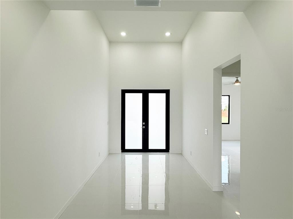 A bright, minimalist entryway features white walls, high ceilings, and a black-framed double glass door — 4005 NW 22ND STREET, CAPE CORAL, FL