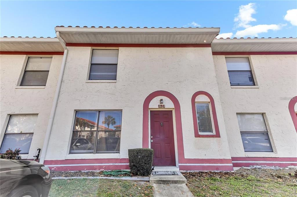 A two-story townhouse exterior features beige stucco walls, red trim, and a red front door — 1631 LITTLE FALLS CIRCLE UNIT 92, ORLANDO, FL