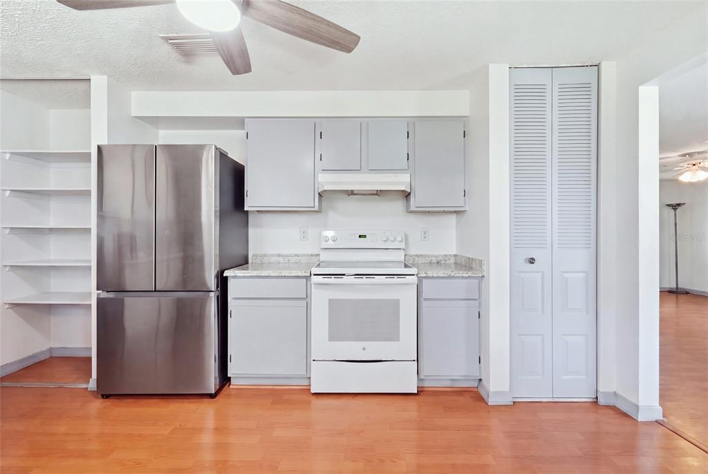 A kitchen features light gray cabinets, a stainless steel refrigerator, a white stove, and wood flooring — 3403 68TH STREET W, BRADENTON, FL