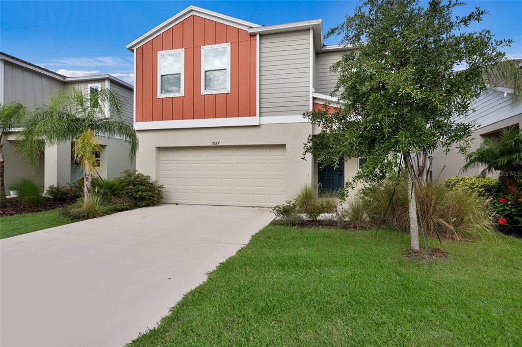 A two-story house features a tan stucco exterior, a two-car garage, and orange vertical siding — 7627 TWINLEAF TERRACE, PARRISH, FL