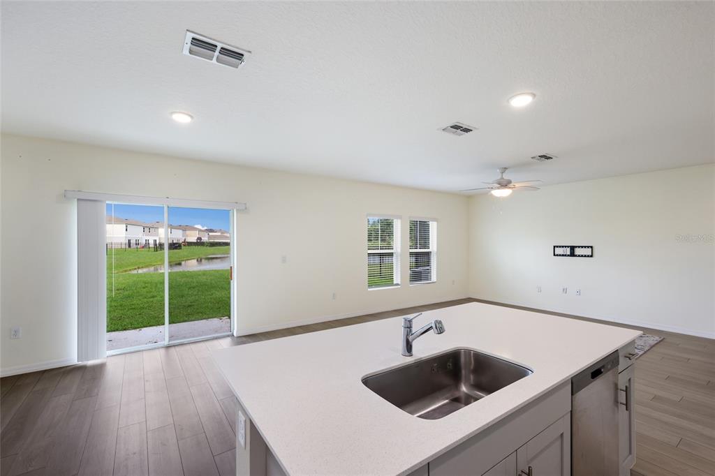 A kitchen island with a sink overlooks an open living area with sliding glass doors — 7627 TWINLEAF TERRACE, PARRISH, FL