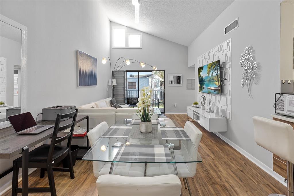 A living and dining area features vaulted ceilings, a glass table, and a wall-mounted television — 3793 ATRIUM DRIVE UNIT L6, ORLANDO, FL