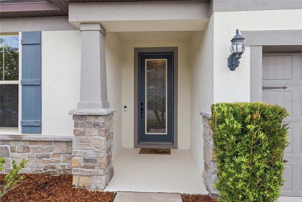 A front entryway features a blue door with glass inlay, stone pillars, and a bush — 18515 CORTES CREEK BOULEVARD, SPRING HILL, FL