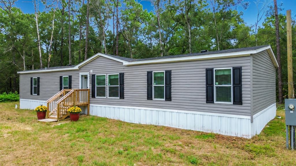 A gray manufactured home with white skirting and a wooden front porch sits in a yard — 10055 W OHIO DRIVE, CRYSTAL RIVER, FL