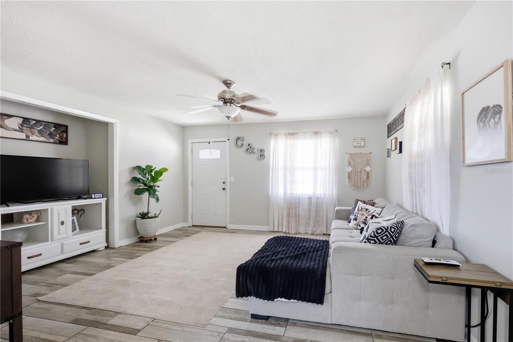 A living room features a light gray sofa, a white media console, and wood-look flooring — 786 E WARREN AVENUE, LONGWOOD, FL