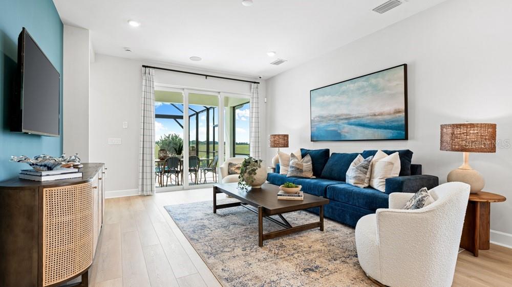 A living room features a blue sofa, a white armchair, and a view of a patio — 26084 ARBOR CIRCLE, PUNTA GORDA, FL