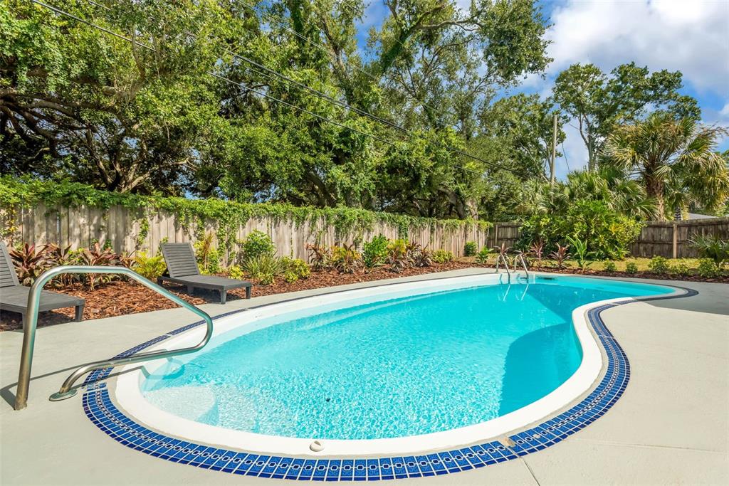 A kidney-shaped swimming pool with a blue tiled border sits in a fenced backyard — 15065 NEWPORT ROAD, CLEARWATER, FL