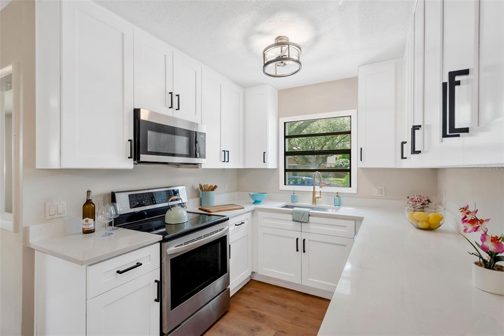 A kitchen with white cabinets, stainless steel appliances, quartz countertops, and a window above the sink — 15065 NEWPORT ROAD, CLEARWATER, FL