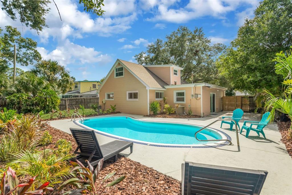 A backyard features a swimming pool, a tan house, and several lounge chairs on a patio — 15065 NEWPORT ROAD, CLEARWATER, FL