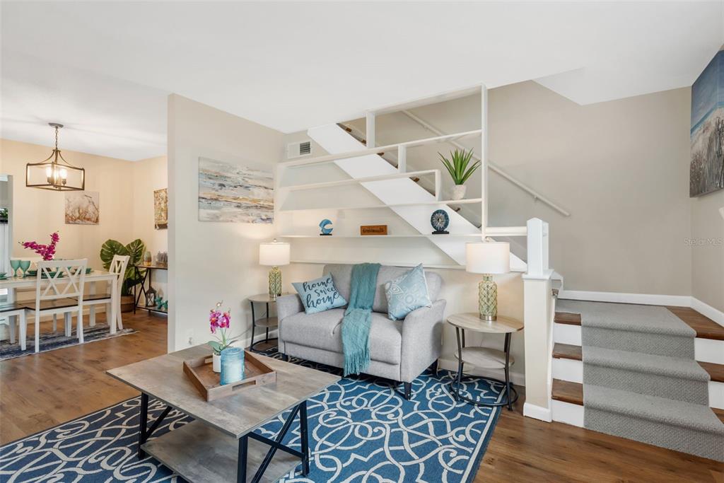 A living room features a grey sofa, a patterned blue rug, and an open staircase — 15065 NEWPORT ROAD, CLEARWATER, FL