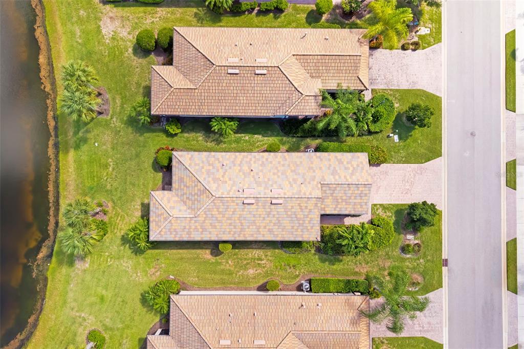 An aerial view shows three suburban houses with tiled roofs situated between a road and water — 6726 HAVERHILL COURT, BRADENTON, FL