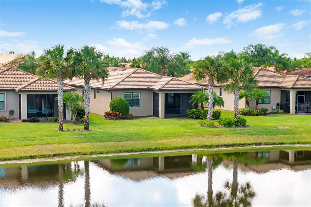 A view of a single-story house with a tiled roof and screened lanai beside water — 6726 HAVERHILL COURT, BRADENTON, FL