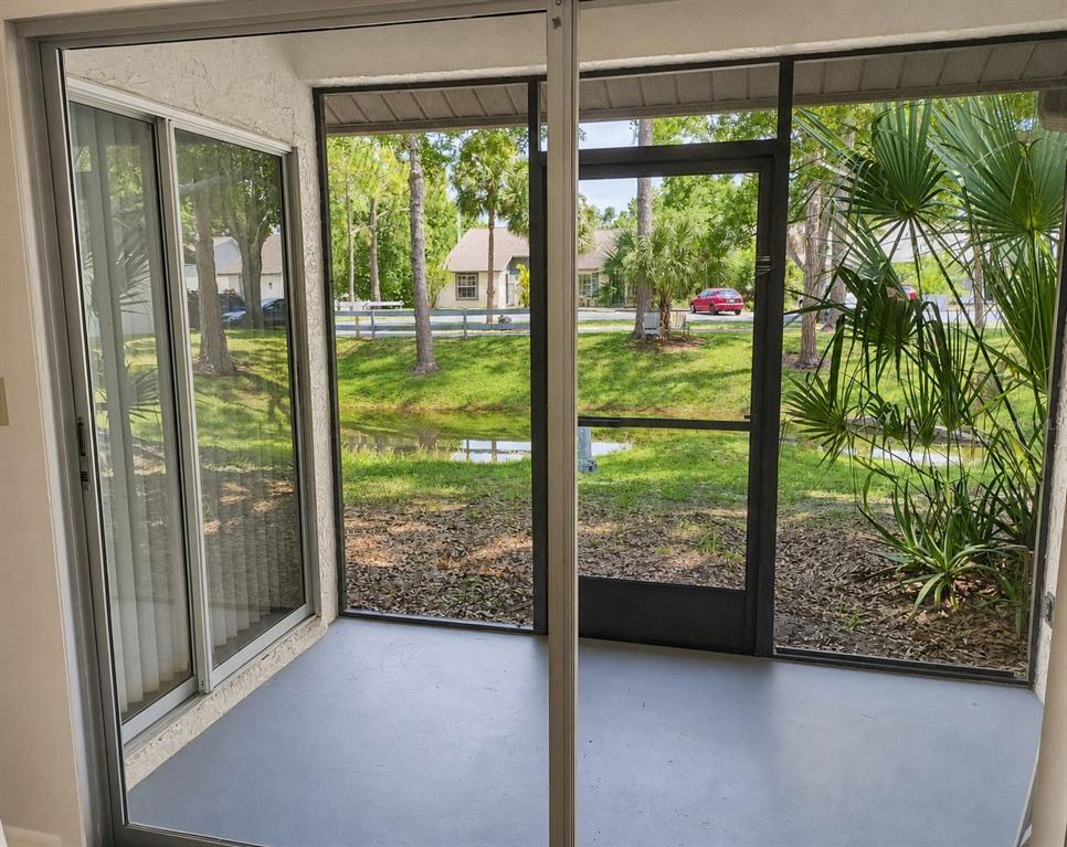 This virtually staged living room features a grey sofa, blue armchairs, and a sliding glass door — 3962 LA COSTA LANE, LARGO, FL