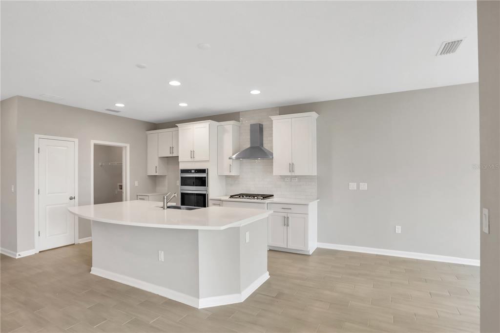 A modern kitchen features white cabinetry, a large center island, and light wood-look flooring — 3157 GADWALL RUN, ORANGE PARK, FL