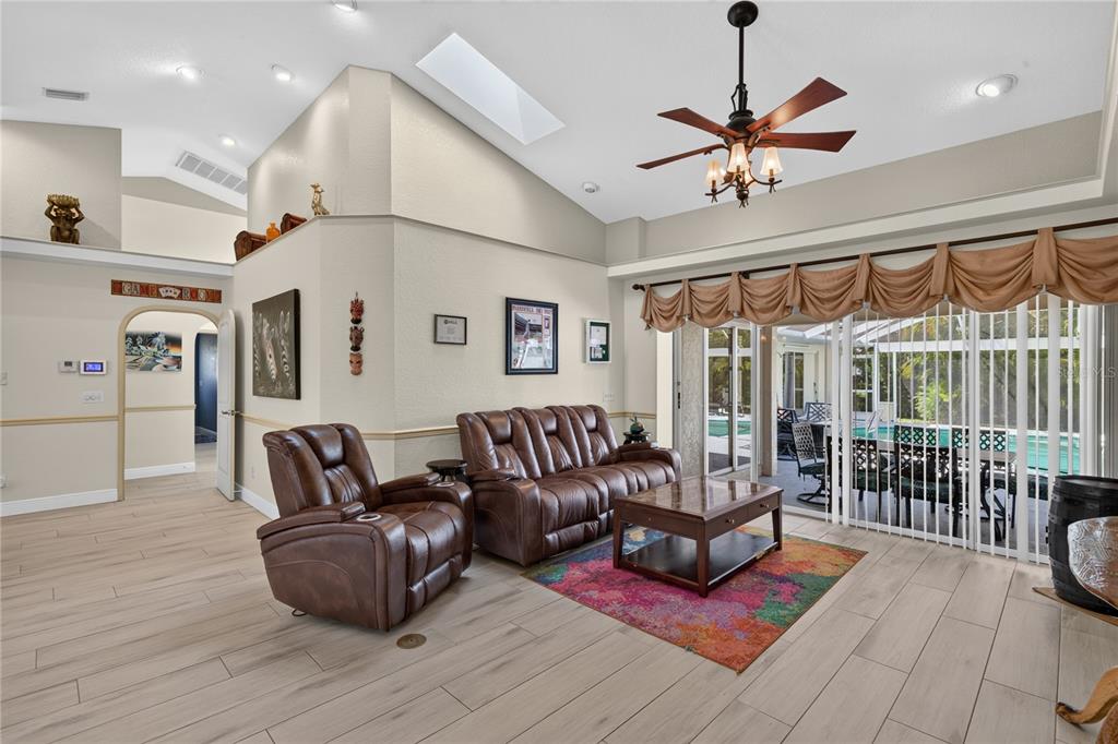 A living room with vaulted ceilings, tile flooring, a leather sofa, and sliding glass doors — 17368 NORSEMAN AVENUE, PORT CHARLOTTE, FL