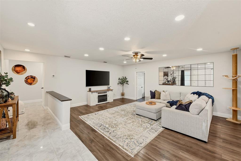 A living room features wood-look flooring, a sectional sofa, a television, and a mirrored wall — 2165 CAMPUS DRIVE, CLEARWATER, FL