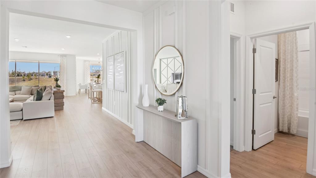 A bright entryway features a console table, round mirror, and wood-look flooring leading to living areas — 3049 CANOPY OAK BOULEVARD, WILDWOOD, FL