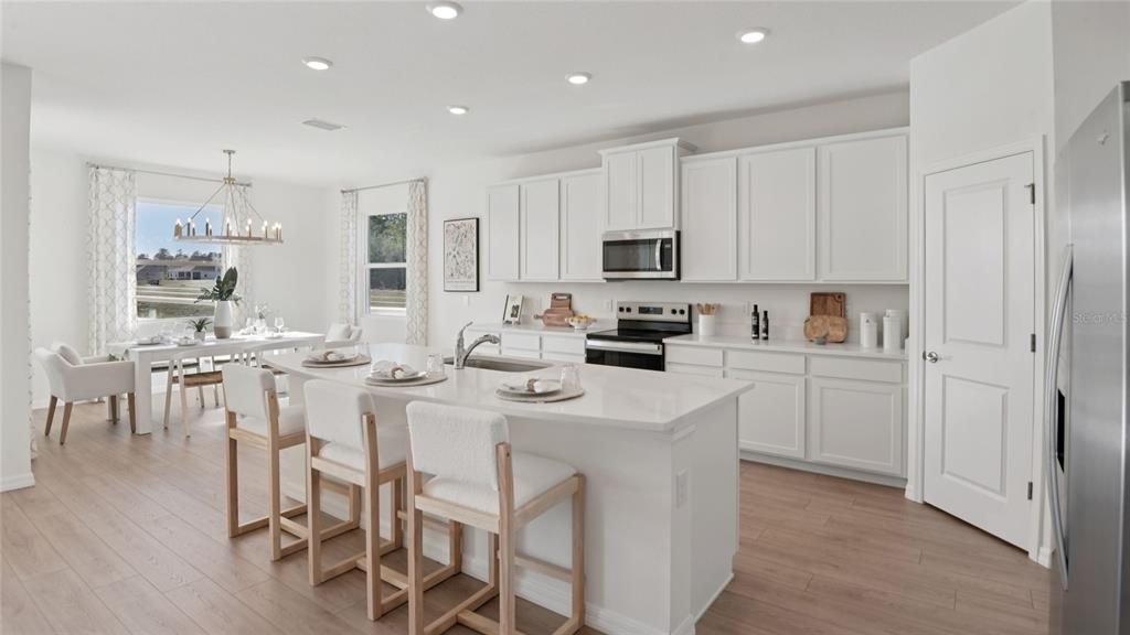 A bright, modern kitchen features white cabinetry, a central island with seating, and light flooring — 3049 CANOPY OAK BOULEVARD, WILDWOOD, FL