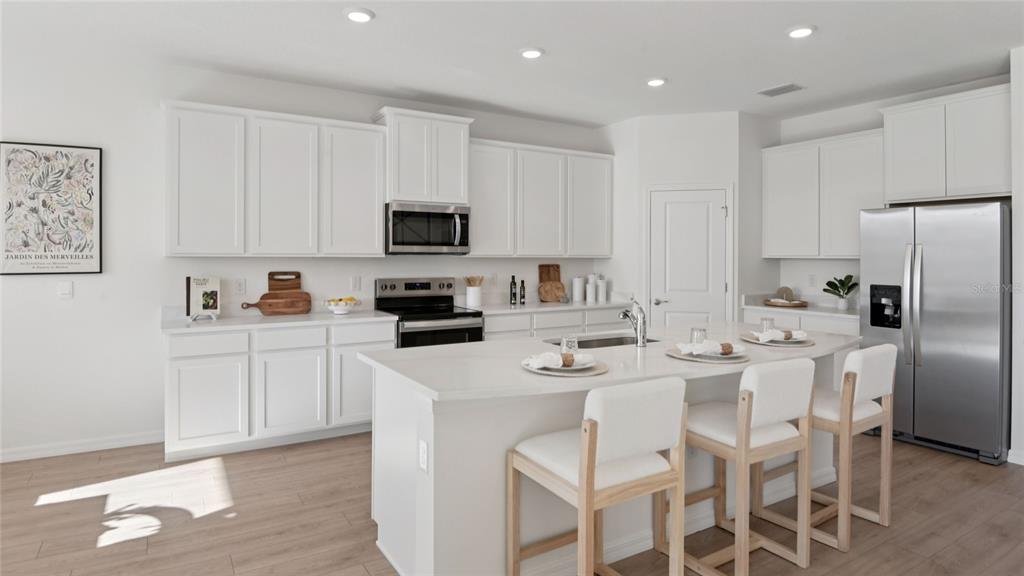 A modern kitchen features white cabinetry, stainless steel appliances, a center island, and light flooring — 3049 CANOPY OAK BOULEVARD, WILDWOOD, FL