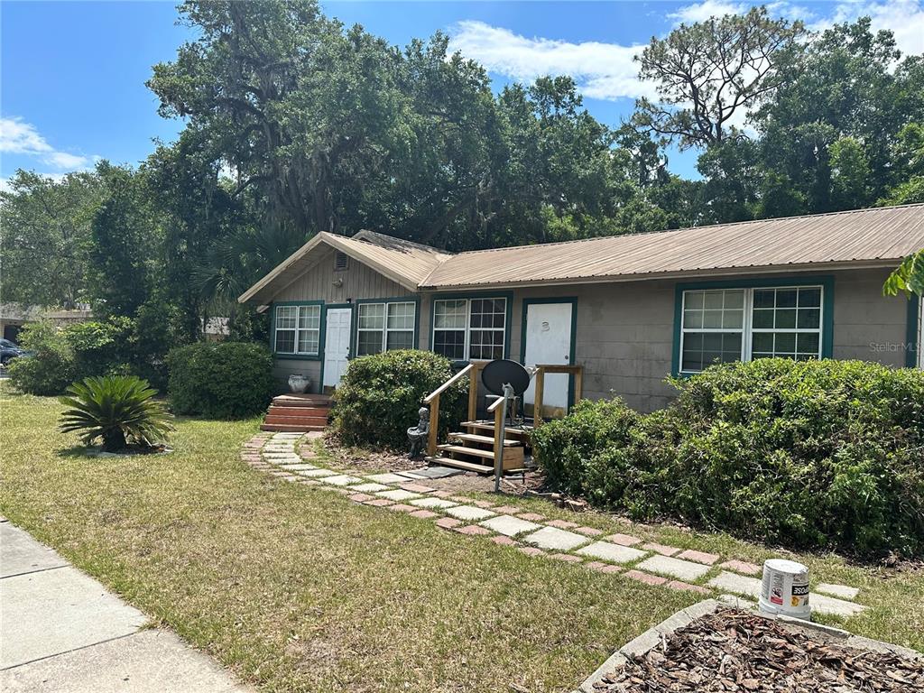A single-story house with a metal roof, green trim, and a stone walkway in front — 919 NW 23RD AVENUE, GAINESVILLE, FL
