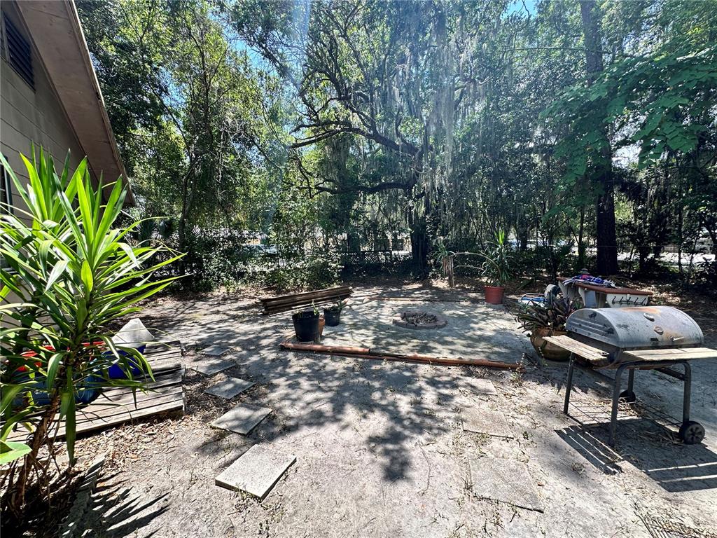 A backyard patio features a fire pit, a grill, and scattered stone pavers under trees — 919 NW 23RD AVENUE, GAINESVILLE, FL