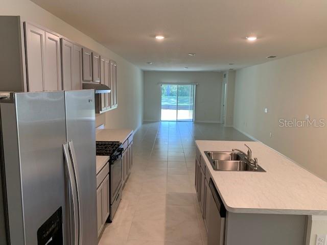 A kitchen with light-colored cabinets, stainless steel appliances, and an island overlooks a living area — 20007 ROYAL TERN COURT, LEESBURG, FL
