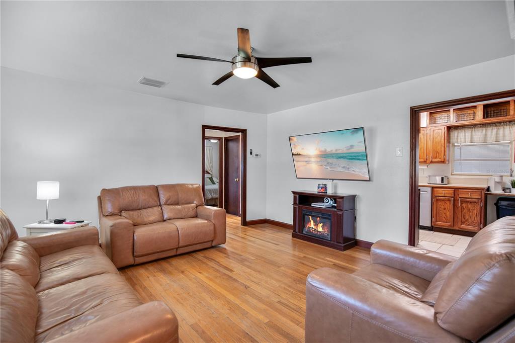 A living room with hardwood floors, leather furniture, a ceiling fan, and a fireplace console — 11 ASTER DRIVE, DEBARY, FL