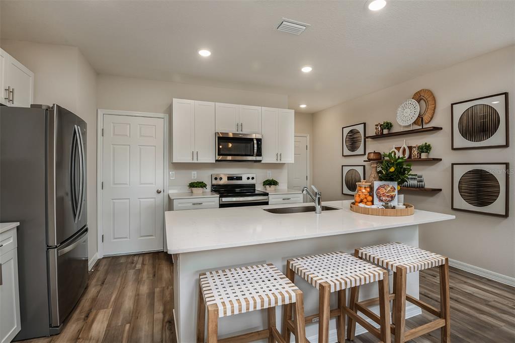 A modern kitchen features white cabinetry, stainless steel appliances, a quartz island, and woven bar stools — 4247 HILLOCK BOULEVARD, HAINES CITY, FL