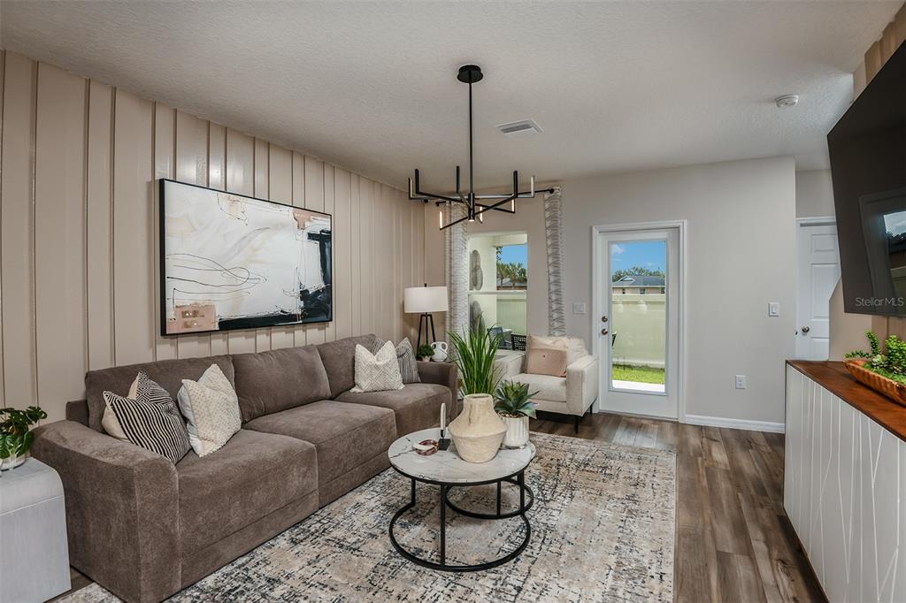 A living room features a brown sectional sofa, a modern chandelier, and vertical wall paneling — 4247 HILLOCK BOULEVARD, HAINES CITY, FL