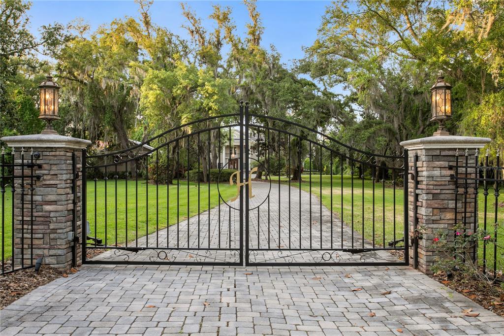A black metal gate with a gold letter H stands between two stone pillars — 9205 POST ROAD, ODESSA, FL