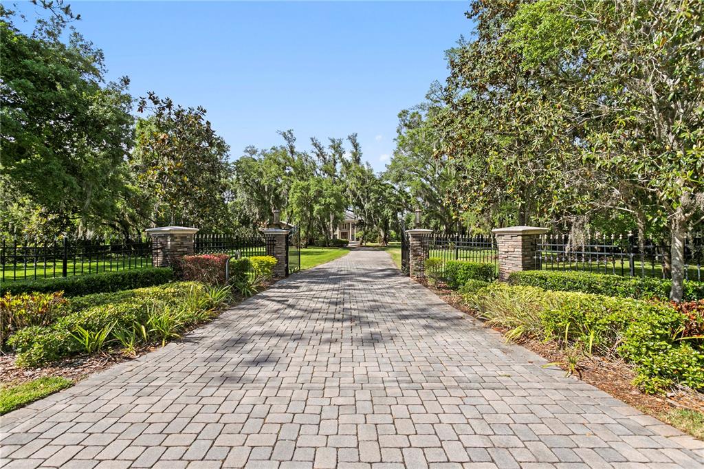 A paved driveway leads through stone pillars and iron gates toward a house among trees — 9205 POST ROAD, ODESSA, FL