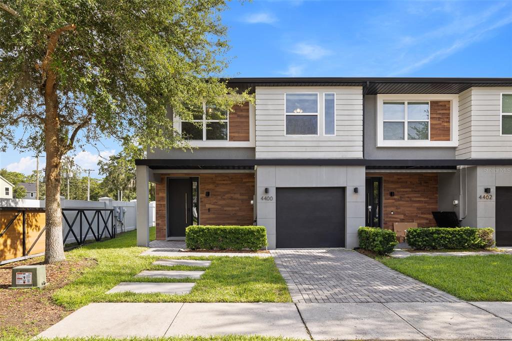 A two-story townhouse exterior with a paved driveway, garage, and wood-paneled accents — 4400 LE REVE COURT, KISSIMMEE, FL