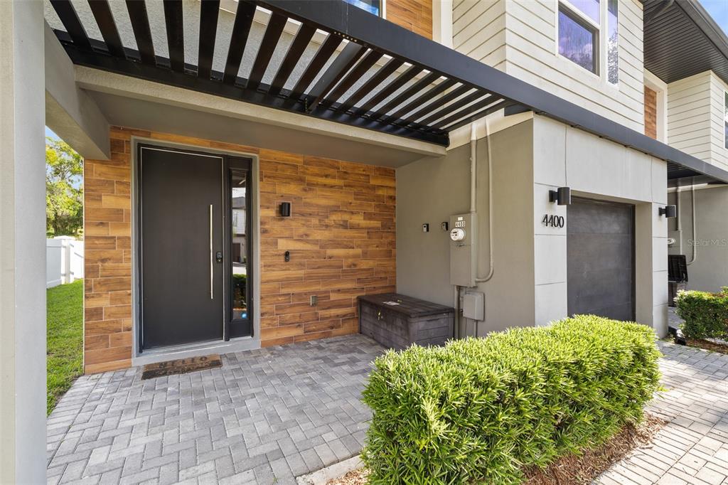 A modern home entrance features a wood-tiled wall, a dark front door, and a paved porch — 4400 LE REVE COURT, KISSIMMEE, FL