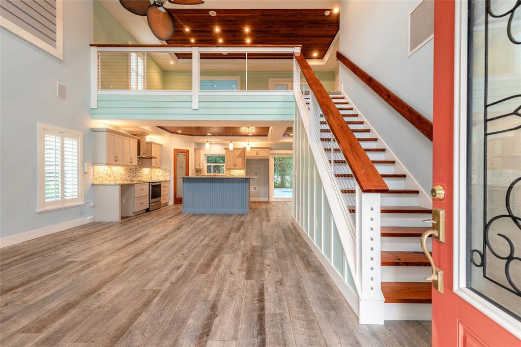 An open-concept living area with a kitchen, wooden staircase, and a lofted upper level — 130 HERNANDEZ AVENUE, ORMOND BEACH, FL