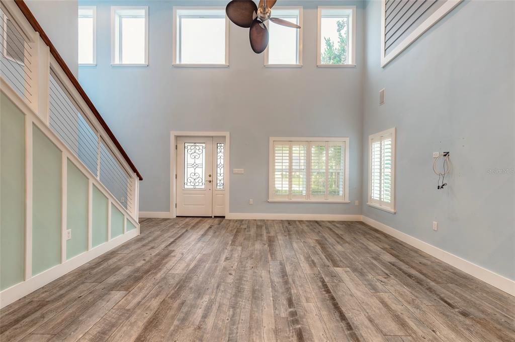 A bright, high-ceilinged entryway features light blue walls, wood-look flooring, and a staircase with railings — 130 HERNANDEZ AVENUE, ORMOND BEACH, FL
