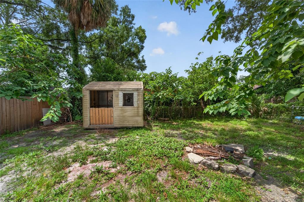 A small, weathered storage shed sits in a grassy backyard with a stone fire pit — 1703 E IDELL STREET, TAMPA, FL