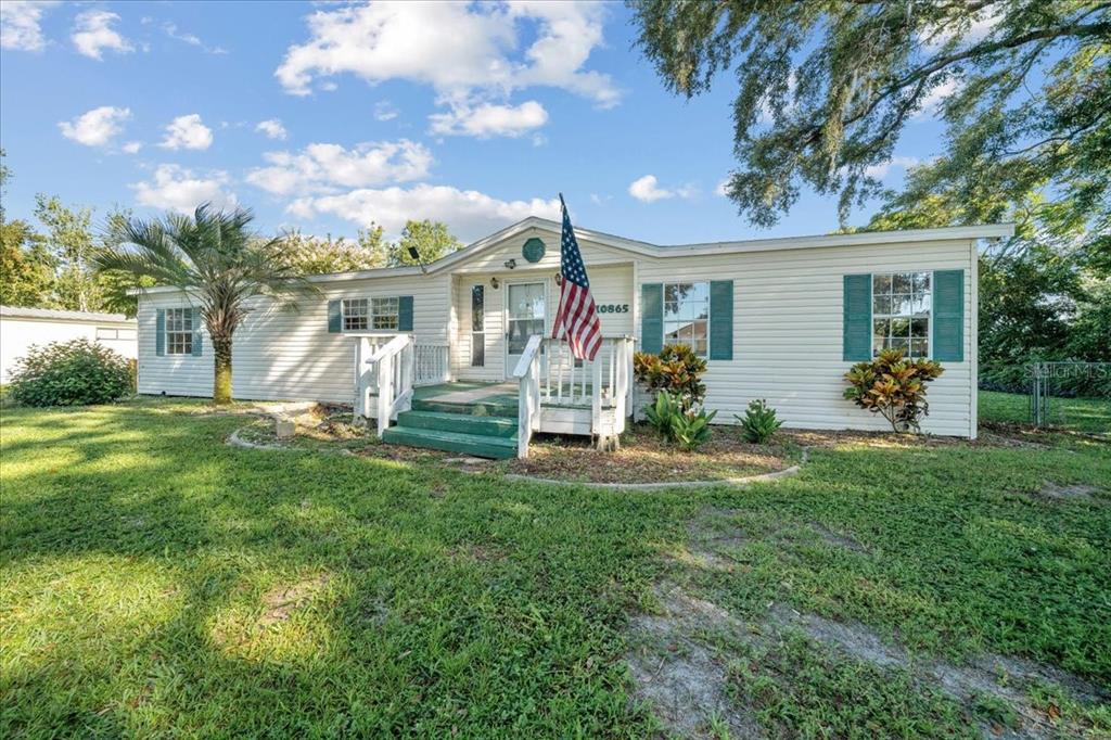 A single-story manufactured home with white siding, green shutters, and a front porch with stairs — 10865 SE TIMUCUAN ROAD, SUMMERFIELD, FL