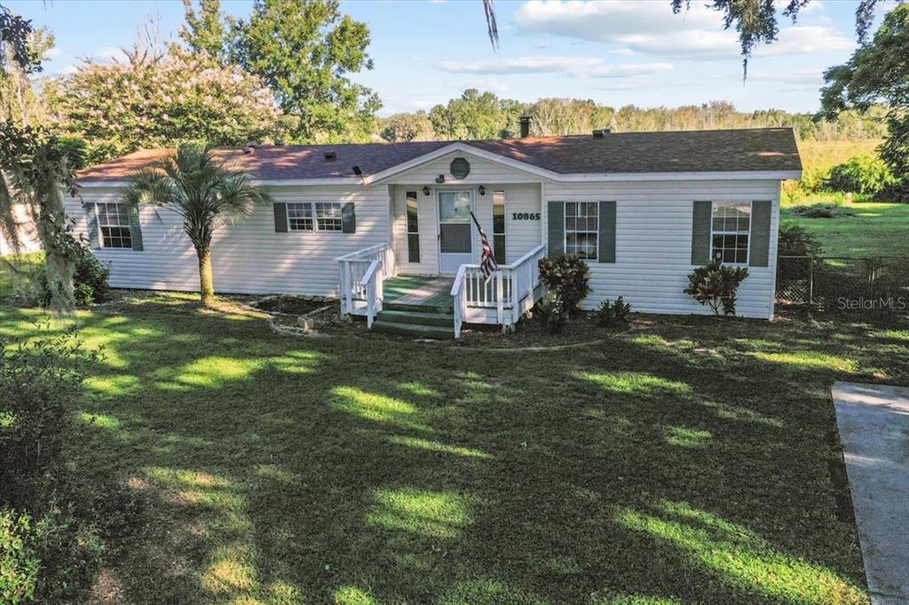 A single-story white house with a gabled entryway and a wooden porch sits on grass — 10865 SE TIMUCUAN ROAD, SUMMERFIELD, FL