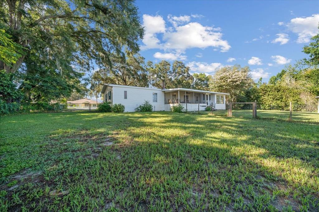 A white single-story house with a screened porch sits on a large, grassy lot — 10865 SE TIMUCUAN ROAD, SUMMERFIELD, FL